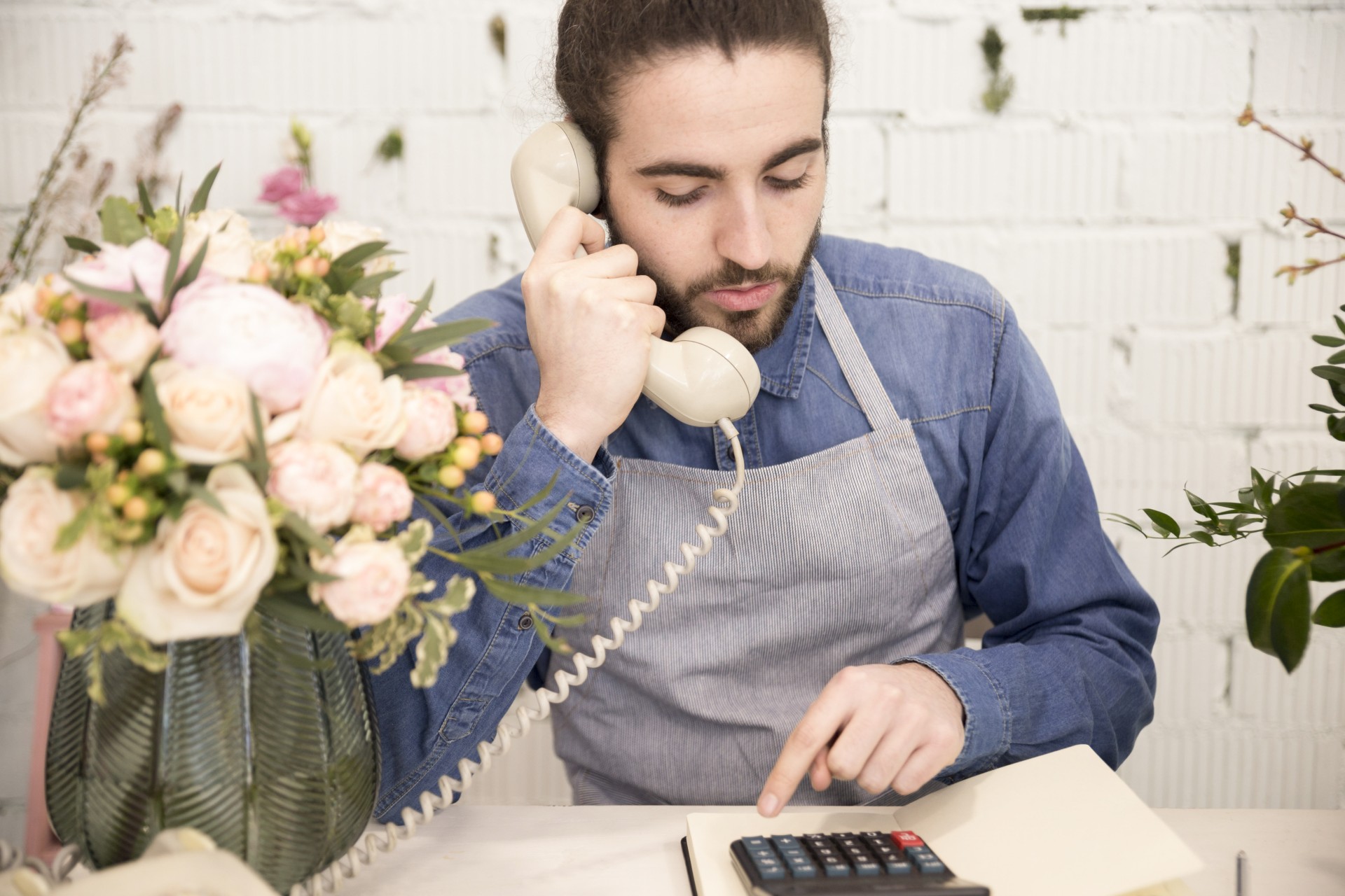 male-florist-using-calculator-while-talking-on-telephone