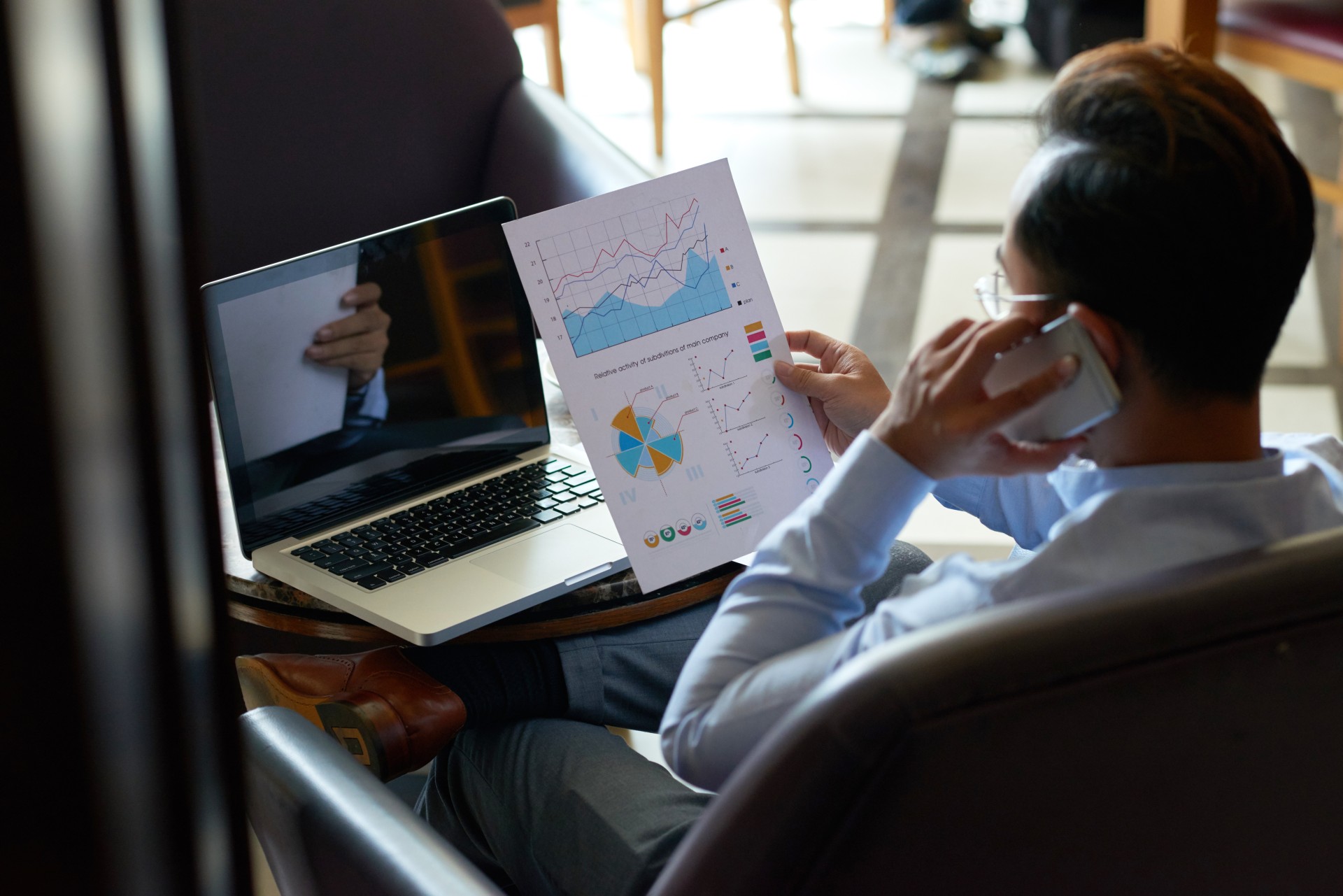 Businessman analyzing financial report in his hand and calling on the phone, view over the shoulder